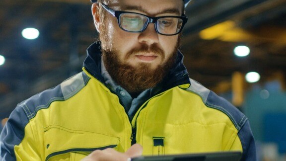 A man wearing a yellow jacket and glasses is intently examining a tablet device