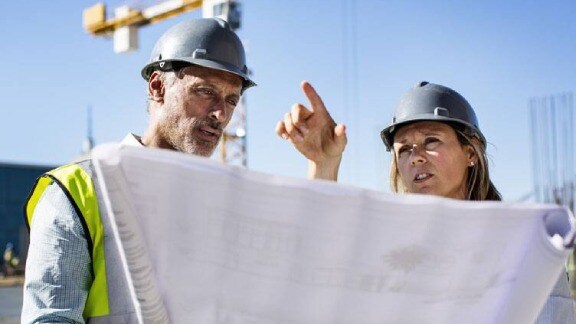 Two workers studying a blueprint while engaged in a construction planning discussion