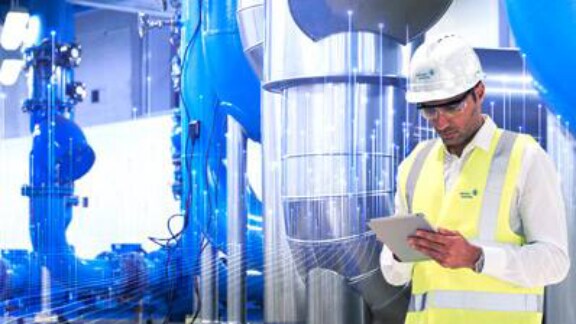A man wearing a hard hat and safety vest is focused on using a tablet in a construction environment