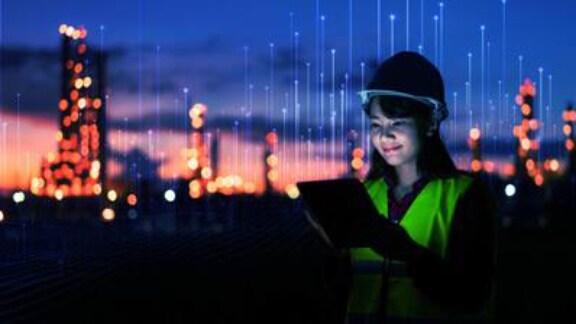 A woman wearing a safety vest and hard hat is holding a tablet computer