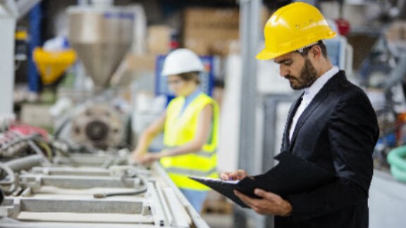 Close up of a worker with the tab in his hand with a blur background of other workers on the manufacturing floor