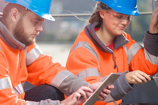 Two construction workers with one looking at the tab while other one fixing with the tool