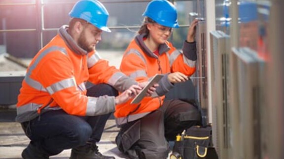 Two construction workers with one looking at the tab while other one fixing with the tool