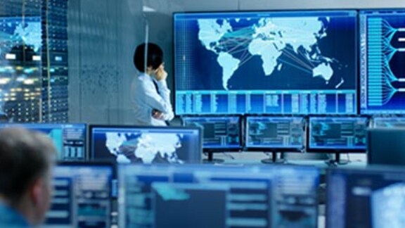 An employee is analysing the feed from the computers on a big screen