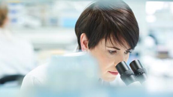 A female scientist closely looking into the microscope